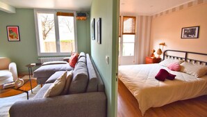 Una habitación con una cama, un sofá y una silla. Hay ventanas y un radiador.