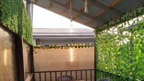 A balcony with a wooden table and two wicker chairs, surrounded by a metal railing and covered with green foliage. - The RISE (Tashkent)