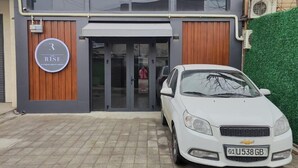 A modern building with a large glass entrance, a sign reading "The Rise", and a white car parked in front. - The RISE (Tashkent)