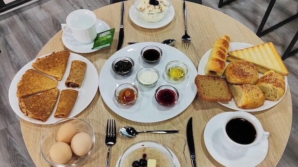 A round dining table with various breakfast items including pancakes, eggs, toast, and condiments. - The RISE (Tashkent)