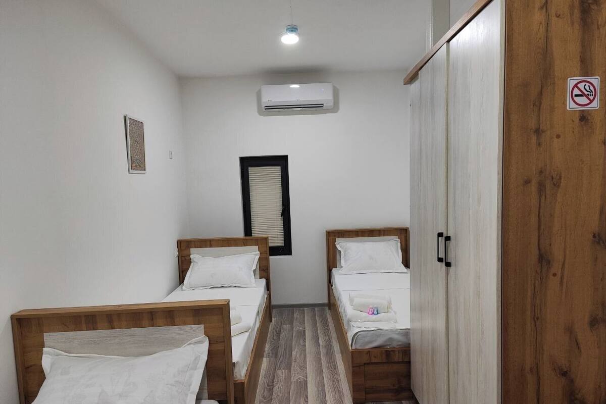A small, clean room with two wooden beds, a wardrobe, and a window with blinds.