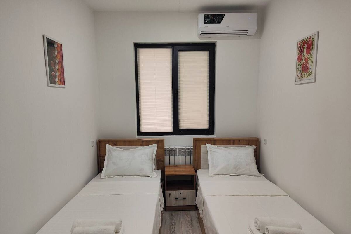 A twin room with two beds, a small wooden nightstand, and an air conditioning unit.