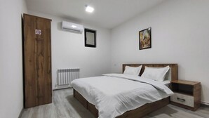 A bedroom with a wooden bed, white bedding, a nightstand, a radiator, and a door with a no-smoking sign. - The RISE (Tashkent)