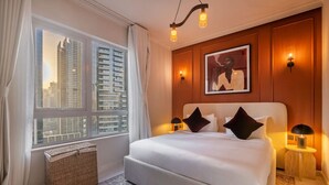 A hotel room with a large bed, a view of tall buildings, and a framed artwork on the wall.