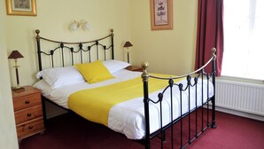 A neatly made bed with a yellow bedspread and a single yellow pillow, a wooden nightstand with a lamp, and a framed picture on the wall. - Victoria Lodge Guest House (Salisbury)