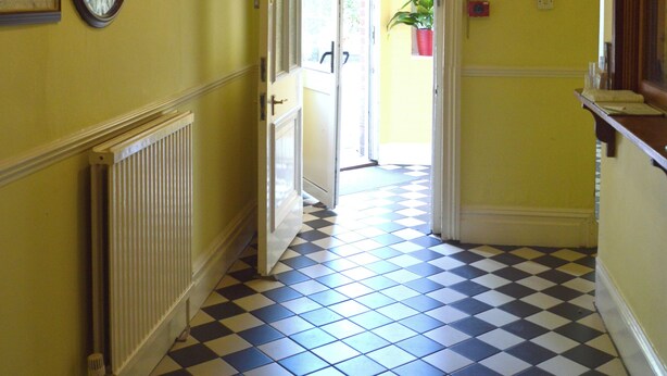 A hallway with a checkered floor, a radiator, a hanging light fixture, and a door leading to another room. - Victoria Lodge Guest House (Salisbury)