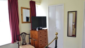 A bedroom with a bed, a wooden dresser, a television, a chair, and a mirror. - Victoria Lodge Guest House (Salisbury)