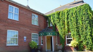 A brick building with a reception area, a green awning, and a large ivy-covered wall. - Victoria Lodge Guest House (Salisbury)