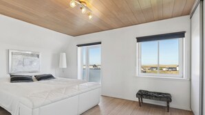 Quarto com cama grande, um banco, janela com vista e luminária no teto.