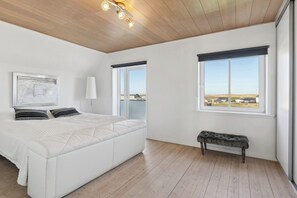 Un dormitorio con una cama grande, un banco, una ventana con vistas y una lámpara en el techo.