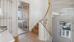 Uma escada com corrimão de madeira e paredes brancas, que leva a um quarto com cama e janela.