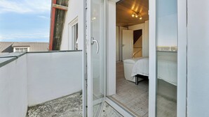 Quarto com uma cama, uma cadeira branca e porta de vidro que dá para área externa.