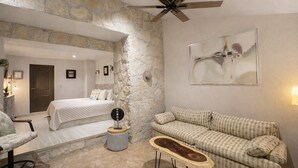A room with a stone wall, a bed, a sofa, and a ceiling fan. - Bremar Collection Boutique Hotel (Celestún)