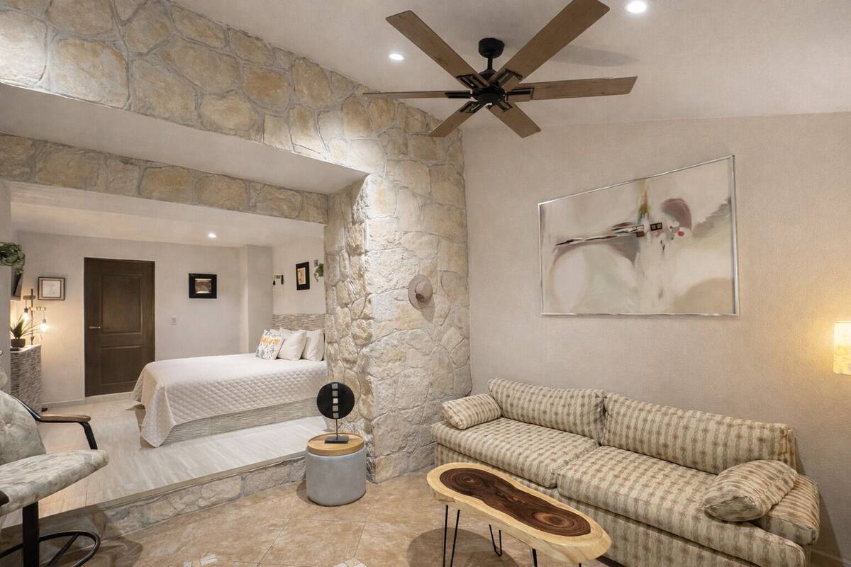 Une pièce avec un mur en pierre, un lit, un canapé et un ventilateur de plafond.