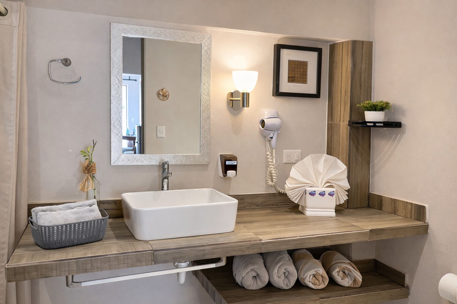Un baño moderno con un lavamanos rectangular, un espejo, un secador de pelo y un perchero para toallas.