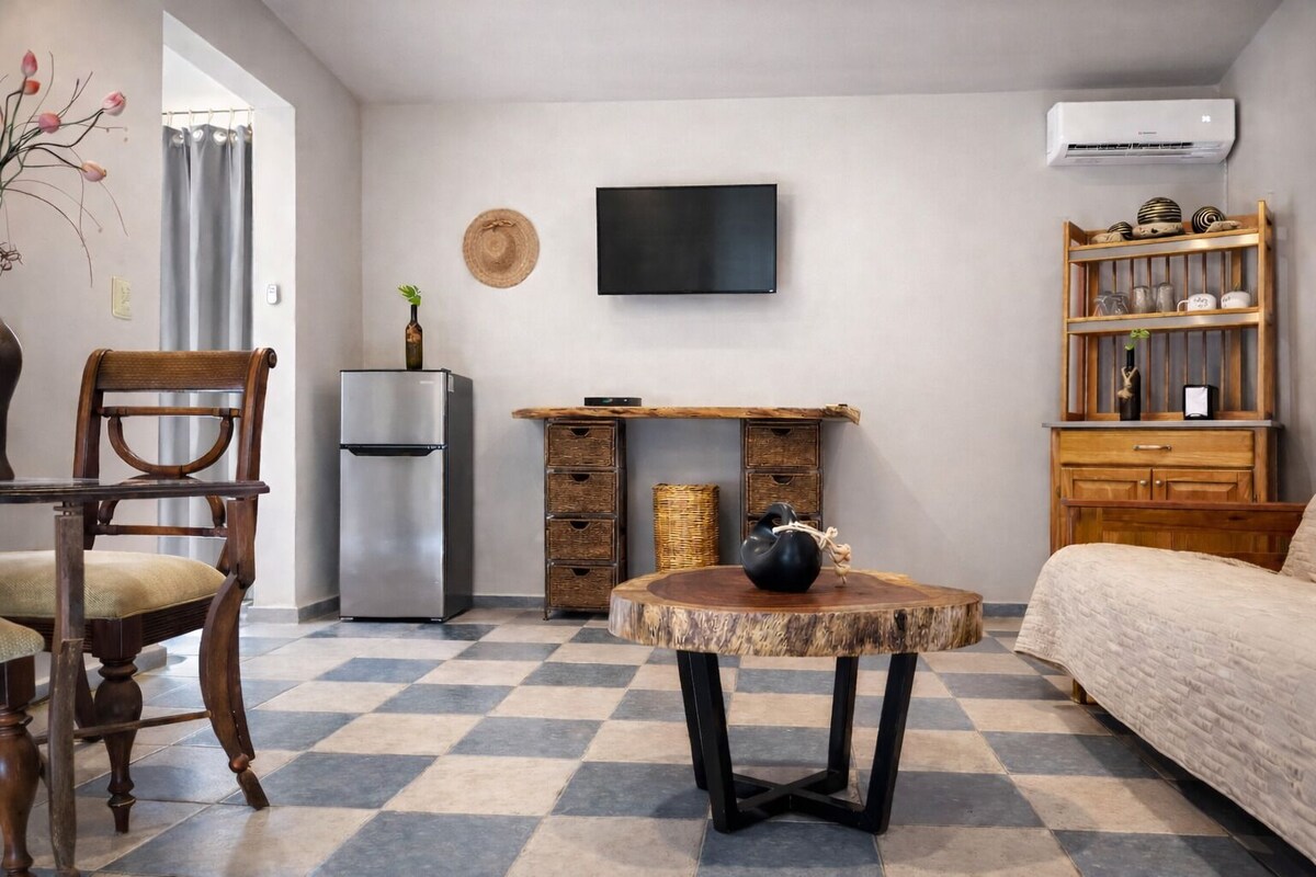 A compact living space with a dining table, a sofa, a TV, a refrigerator, and a bookshelf.