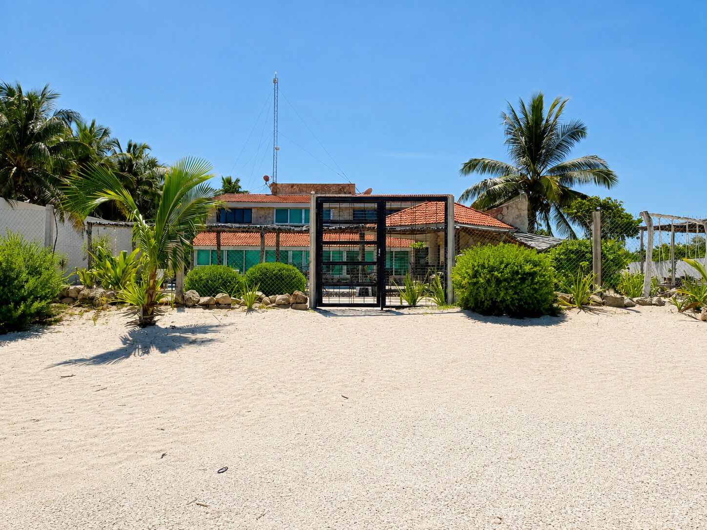 A beachfront property with a gated entrance, a building with a red-tiled roof, and palm trees.