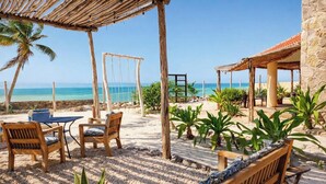 A beachside patio with wooden furniture, a swing, and a stone building. - Bremar Collection Boutique Hotel (Celestún)