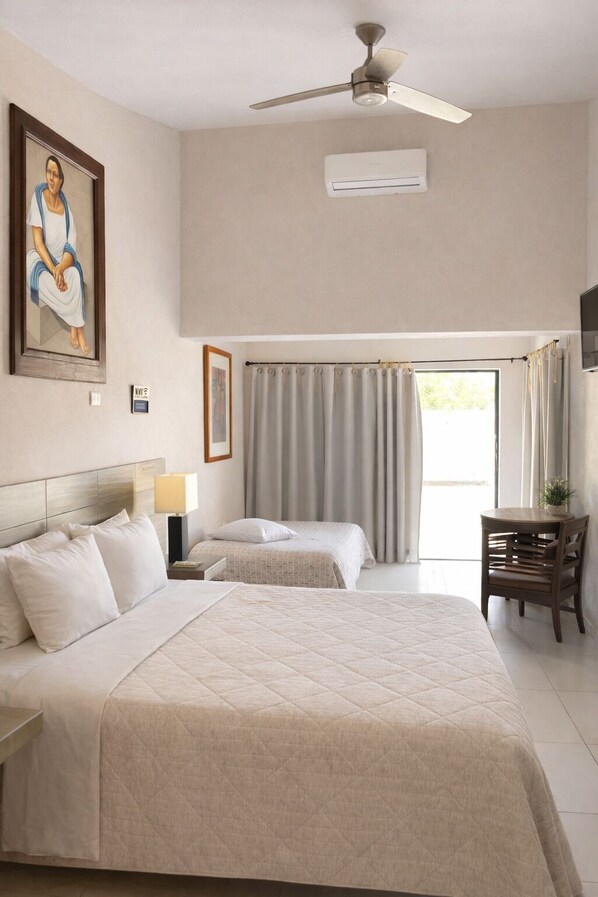 A hotel room with a bed, a desk, a chair, a ceiling fan, and a window with curtains. - Bremar Collection Boutique Hotel (Celestún)