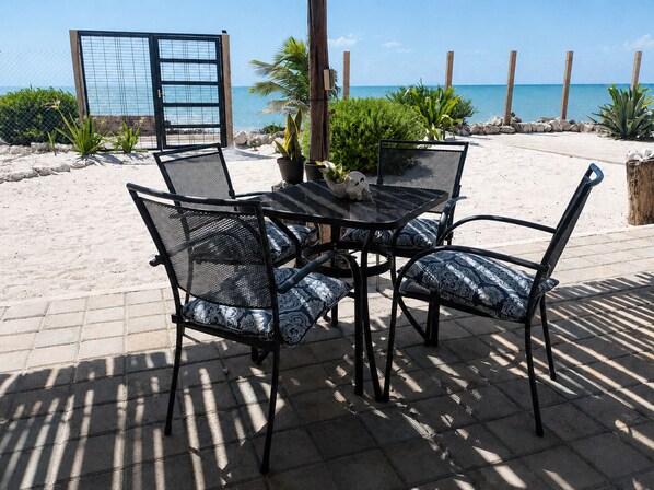 Eine Terrasse mit Tisch und Stühlen, Blick auf den Strand und einem Zaun.