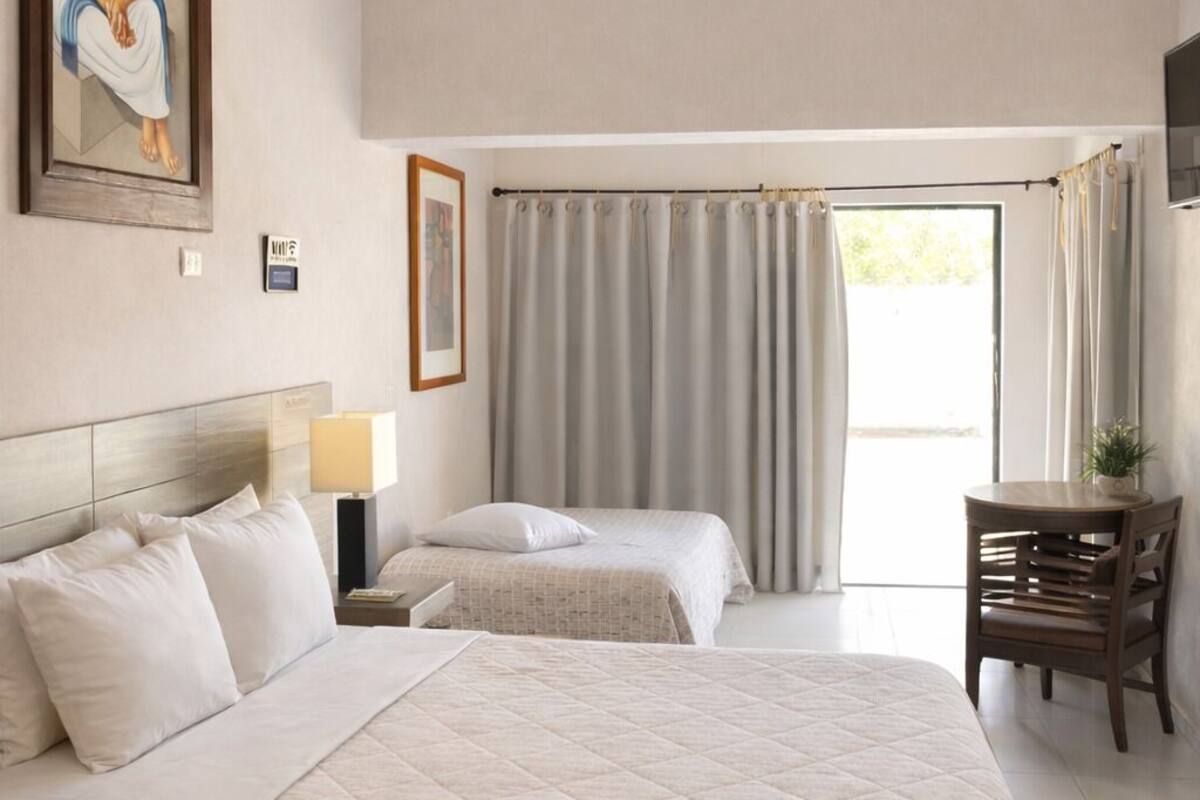A hotel room with a bed, a desk, a chair, a ceiling fan, and a window with curtains.