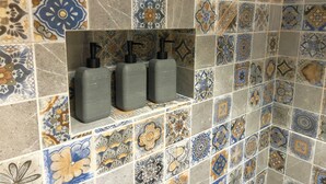 A bathroom with a tiled wall featuring a variety of patterns and a shelf with three gray dispensers. - Bremar Collection Boutique Hotel (Celestún)
