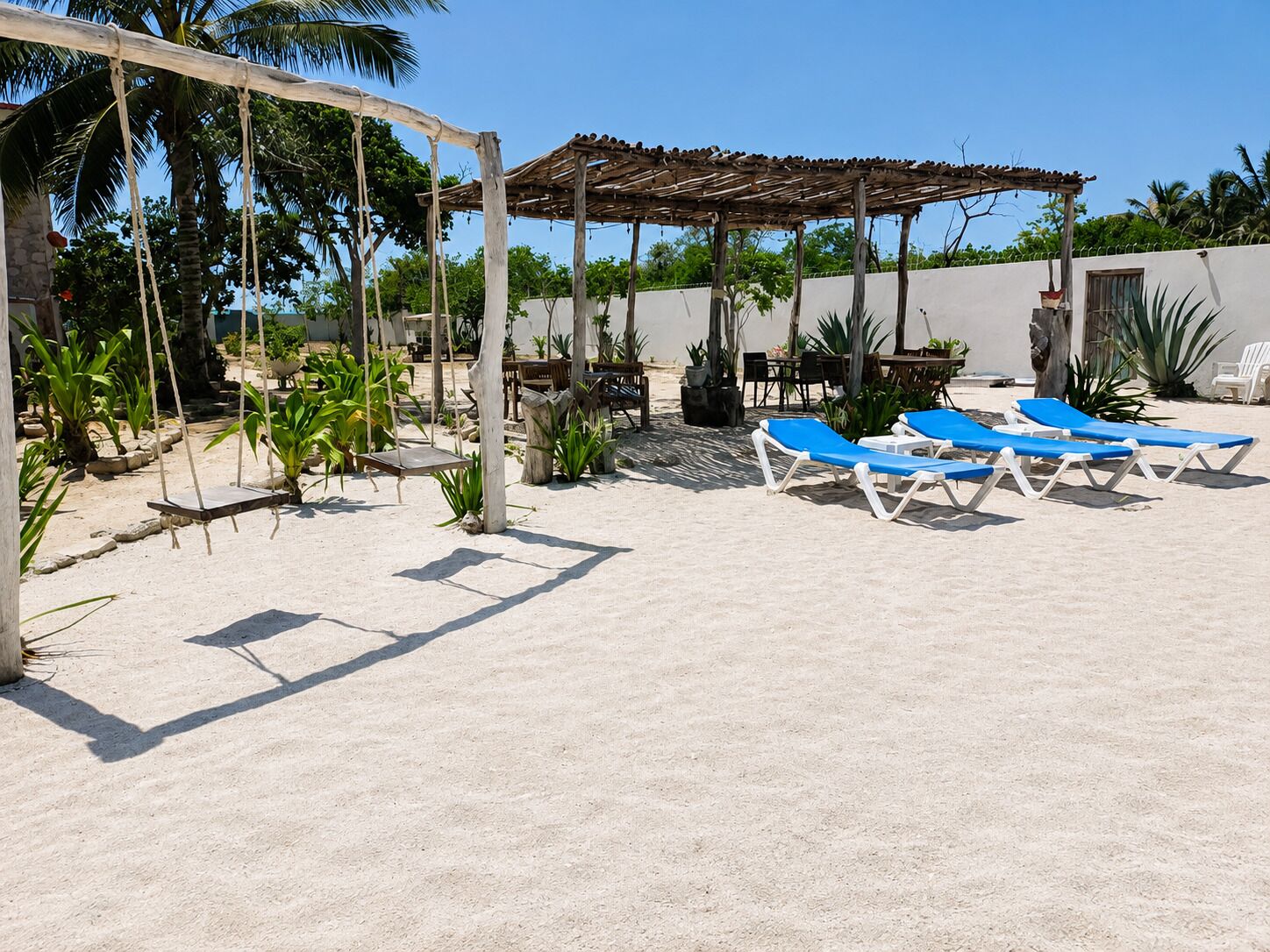 Un patio frente a la playa con una pérgola de madera, sillones de descanso y plantas en macetas.