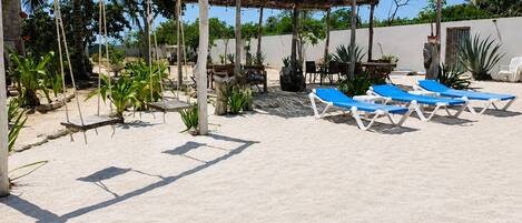 Un patio frente a la playa con una pérgola de madera, sillones de descanso y plantas en macetas.