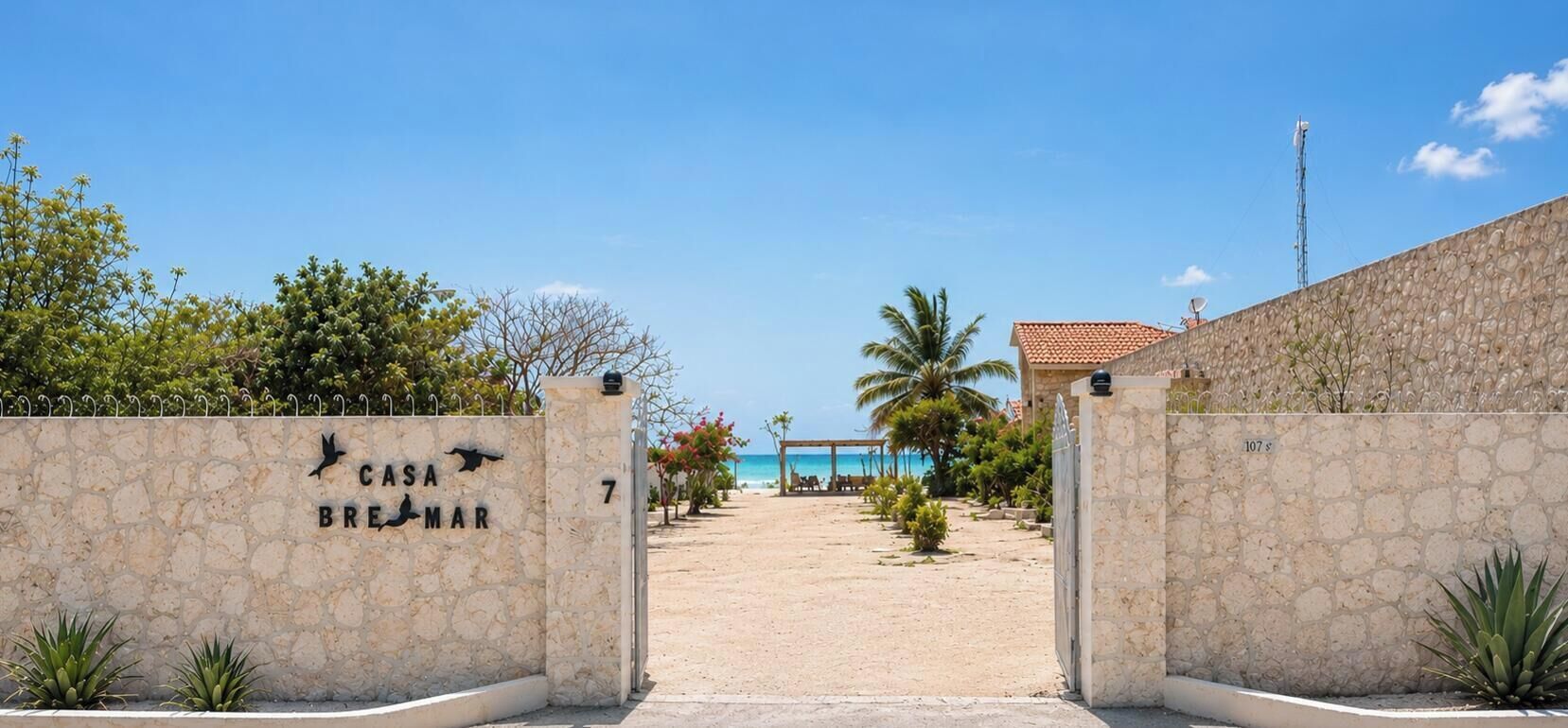 Una puerta de piedra con un letrero que dice 'Casa Brejomar' da acceso a una playa con vista despejada del océano.