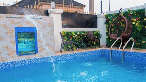A swimming pool with a water feature, a hanging chair, and a wall with a floral design. - AZ KINGS HOTEL AND APARTMENT (Benin City)