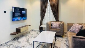 A modern living room with a flat-screen TV mounted on the wall, a sofa, a coffee table, and a marble-patterned floor. - AZ KINGS HOTEL AND APARTMENT (Benin City)