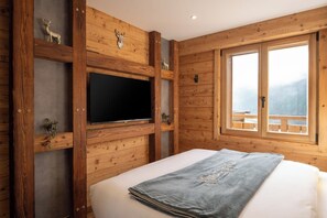 A wooden-paneled room with a bed, a mounted television, and a window with a view of a balcony.