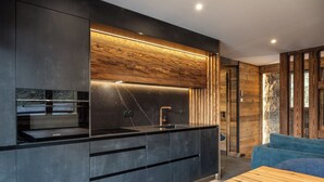 A modern kitchen with a built-in oven, a sink, and a wooden accent wall. - Chalet Le Mirador - Sauna - Hammam (Ventron)