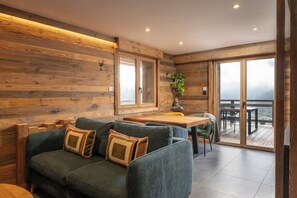 A modern interior with a wooden wall, a sofa with cushions, a dining table, and a view through a glass door.