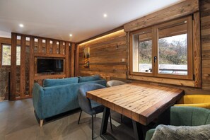 A modern interior with a wooden wall, a flat-screen TV, a blue sofa, and a wooden dining table.