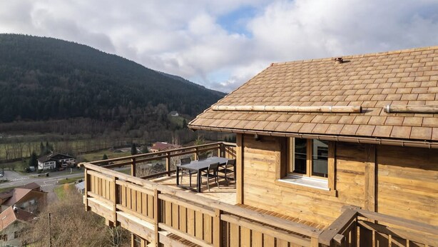 A wooden cabin with a balcony, a view of a valley, and a mountain in the background. - Chalet Le Mirador - Sauna - Hammam (Ventron)