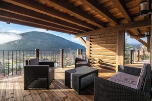 Eine Holzterrasse mit Korbmöbeln, Blick auf einen Berg und einem Geländer.