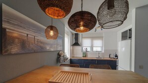 A modern kitchen with a wooden dining table, hanging wicker pendant lights, and a large abstract painting on the wall.
