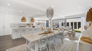 Una cocina moderna con armarios blancos, un comedor con una mesa grande y sillas, y una sala de estar con un sofá y una mesa de centro.