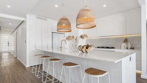 Una cocina moderna con armarios blancos, una isla central con taburetes y luminarias colgantes.