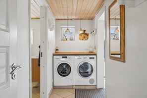 A laundry room with two washing machines, a wooden ceiling, and a mirror on the wall.
