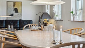 A dining table with a white tablecloth, candles, and glassware. There is a sofa and a lamp in the background. - Cozy holiday home in Harboøre (Harboøre)