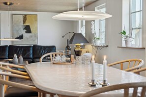 A dining table with a white tablecloth, candles, and glassware. There is a sofa and a lamp in the background.