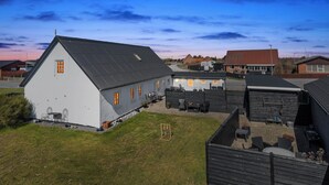 A white building with a sloped roof, a paved courtyard with outdoor seating, and a clear sky. - Cozy holiday home in Harboøre (Harboøre)