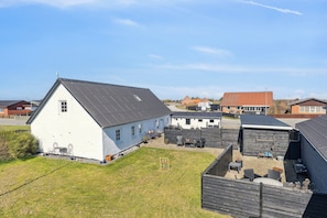 A white building with a sloped roof, a fenced yard with outdoor seating, and a clear sky. - Cozy holiday home in Harboøre (Harboøre)