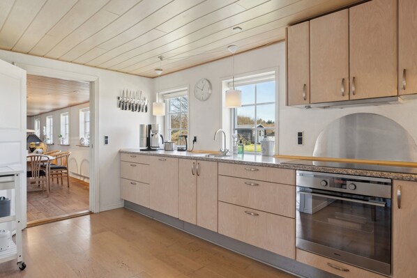 A modern kitchen with wooden cabinets, a stainless steel oven, and a dining area with a table and chairs.
