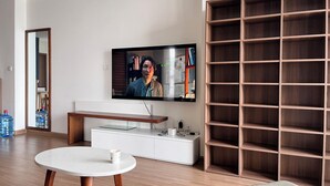 Una sala de estar moderna con un televisor de pantalla plana montado en la pared, una mesa redonda blanca con una taza, un banco de madera y una amplia estantería de madera.