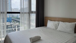 Habitación de hotel con una cama grande, ropa de cama blanca y vistas a un paisaje urbano a través de cortinas translúcidas.