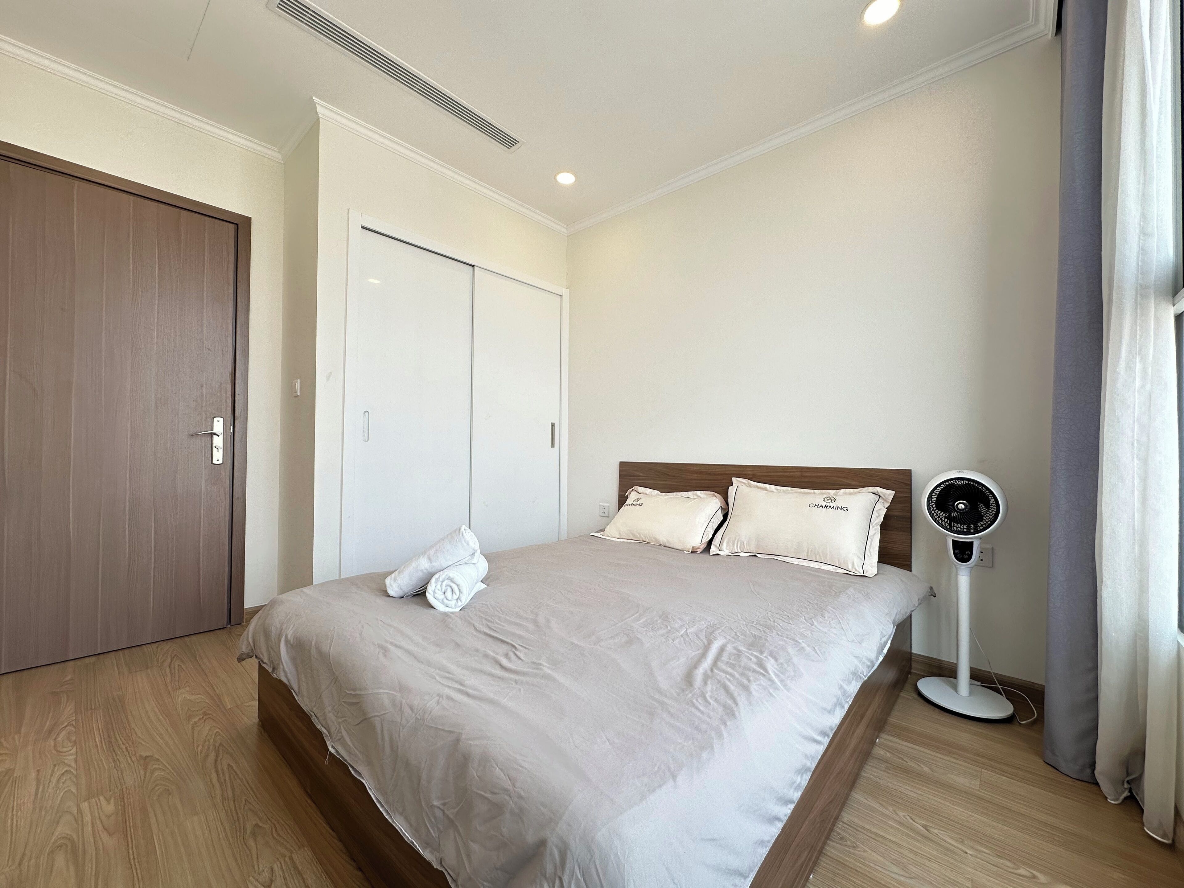 A hotel room with a bed, a bedside fan, and a wardrobe.