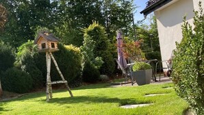 Un jardín con una casita de juegos de madera, un columpio y una zona de patio con muebles de exterior.